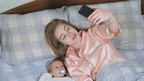 Close up of mother and her newborn baby making video call to father or relatives in a bed. Concept of technology, new generation, family