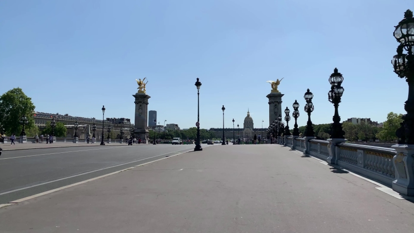 Footage of people walking, cars passing on famous bridge called "Pont Alexandre III" in Paris. It is a sunny summer day. Camera moves forward.