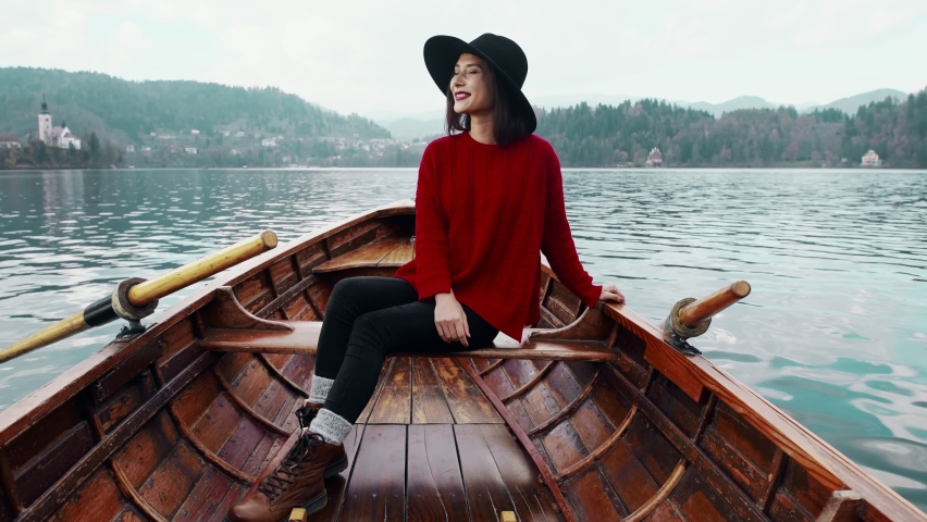 Pretty young girl sitting in boat and looking for the inspiration at background of the Alph mountain view. Happy asian woman relaxing in boat on the beautiful summer lake during her vacation.