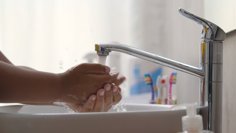 Close up of african child using liquid soap and washing hands in bathroom. Afro-american kid cleaning hands with antibacterial soap in sink. Healthcare and hygiene concept