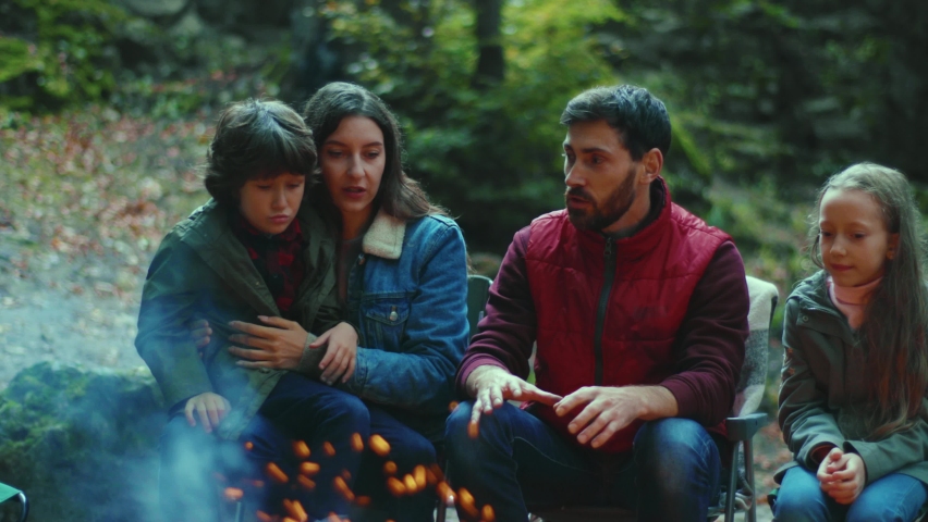 In evening family sits near campfire on autumn tells scary stories. Children with their parents are resting in the woods. Childhood relationship camping. Close up. Slow motion Royalty-Free Stock Footage #1062262204