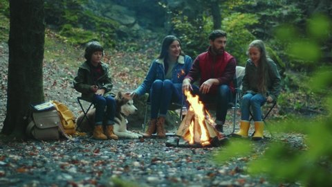 Portrait family sits near campfire on autumn evening. Children with their parents are resting in the woods. Childhood relationship camping. Close up. Slow motion