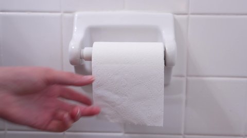 This close up video shows anonymous hands taking toilet paper from a wall mounted toilet paper roll dispenser.