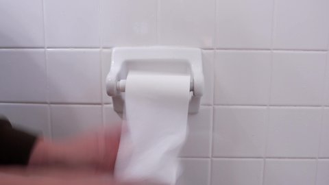 This close up video shows anonymous hands of someone suffering from diarrhea as they frantically pull toilet paper from dispenser.