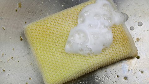 Close video of cleaning a stainless steel pan with soap and a mesh sponge.