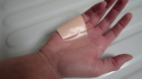 This closeup video shows anonymous hands peeling a large band aid off of a wounded hand.