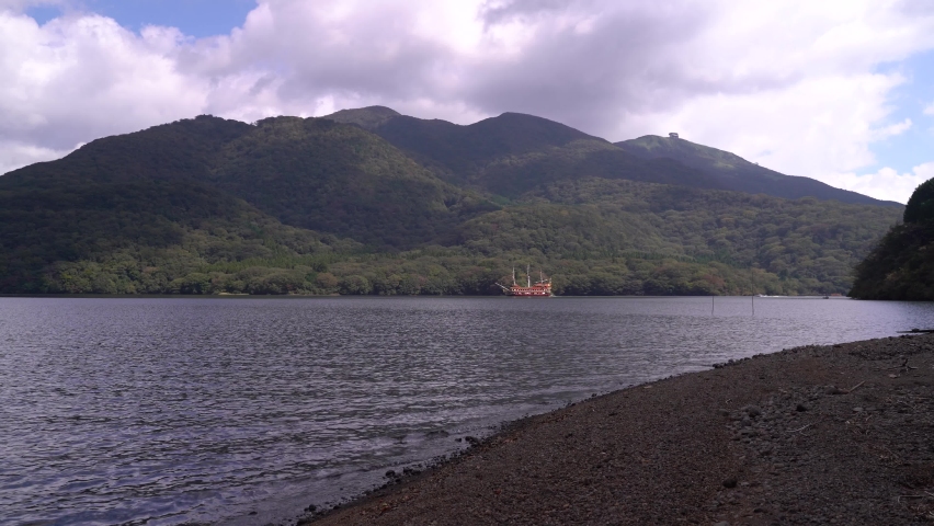 Male Hiker walking into frame at Hakone Lake, waving at famous Pirate Ship in distance