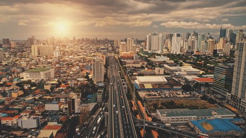Cityscape at sun light with cross highway, streets, skyscrapers aerial. Bridge traffic road with driving cars at summer sunny day. Philippines capital of Manila town at cinematic drone shot