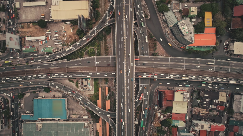 Slow motion top down of cross road traffic with cars, trucks, vehicles in aerial view. Downtown of Manila city with colorful buildings roofs at roadside. Philippines urban lifestyle with local journey