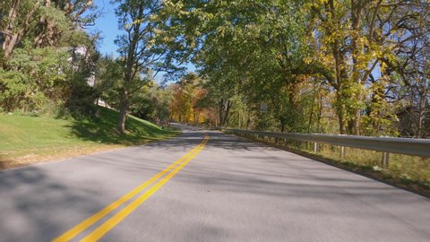 POV Driving a car going up on curvy asphalt Vermont road with colorful trees in fall season. Sunny day with blue sky 