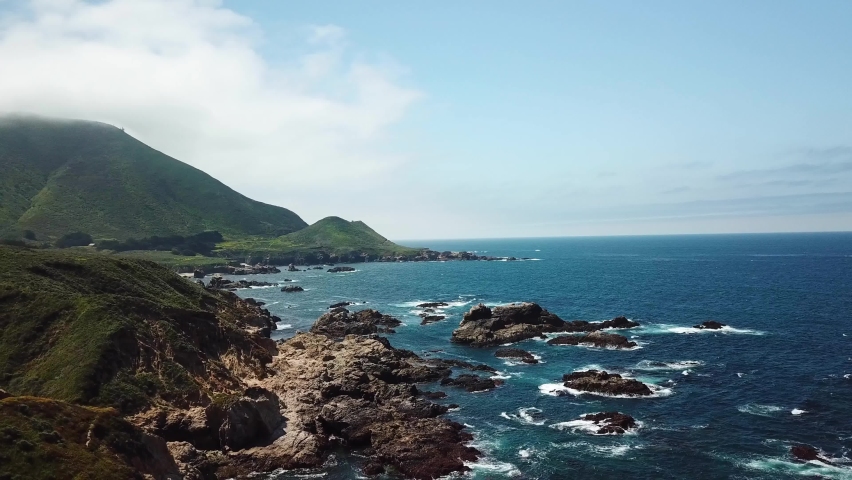 Rocky Coast of Big Sur California State Park with rocks hit by ocean waves, Aerial pan left reveal shot