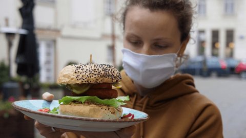 Take away food on the go outdoors during second wave covid-19 pandemic. Casual woman in reusable mask ordered veggie burger served on ceramic plate in street food restaurant