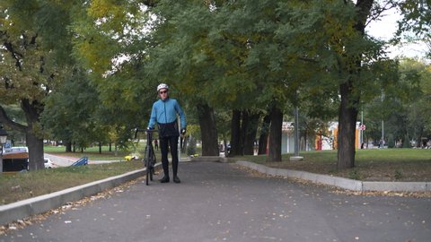 A young man in a bicycle walks through the park. Healthy lifestyle concept