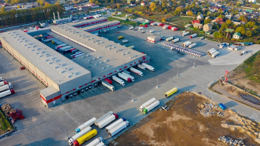 Aerial hyper lapse (motion time lapse) of the logistics park with a warehouse - loading hub. Semi-trucks with freight trailers standing at the ramps for loading/unloading goods at sunset.  Royalty-Free Stock Footage #1062288103