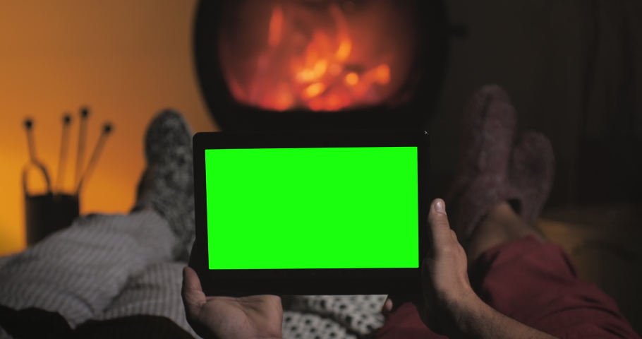 Relaxed couple rest on the sofa in front of fireplace watch green screen tablet wearing woollen socks,winter christmas scene,holding chroma key screen display by the fire place Royalty-Free Stock Footage #1062294541