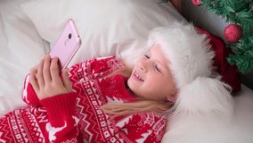4k Christmas online congratulations. Smiling girl using mobile phone for video call. Child talking friends and parents.