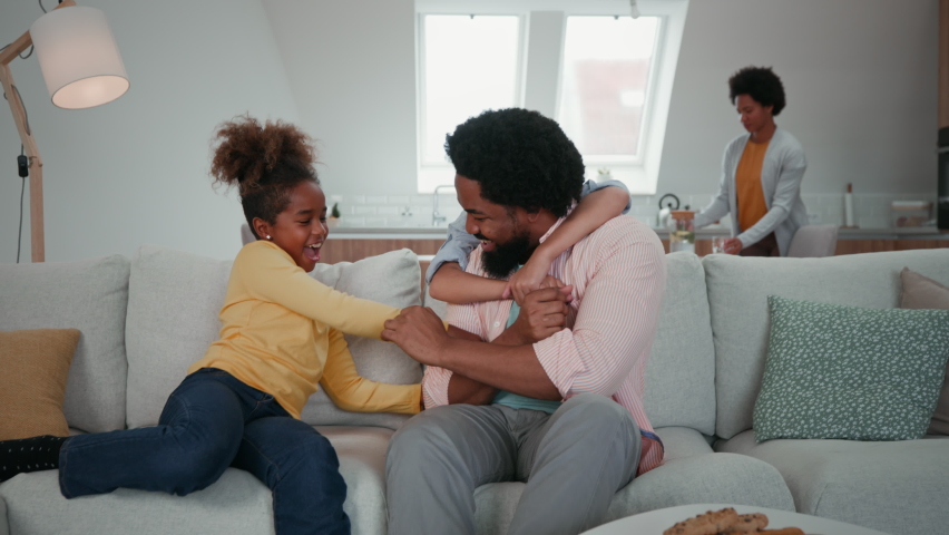 Afro father and children spending weekend together at home and having fun while tickling