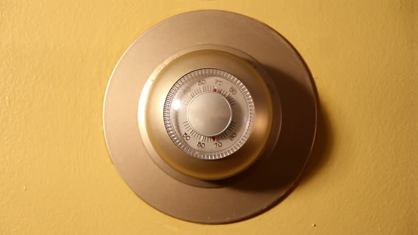 Close-up of a man adjusting an indoor wall thermostat.