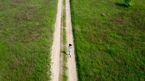 European Woman Running on a dirt road in Summer, slow mo - tracking shot. Extreme Long Shot of dirt road along which the girl runs.