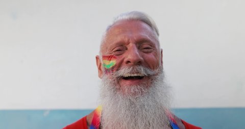 Senior gay man smiling in front of camera with rainbow colors painted on face - Slow Motion