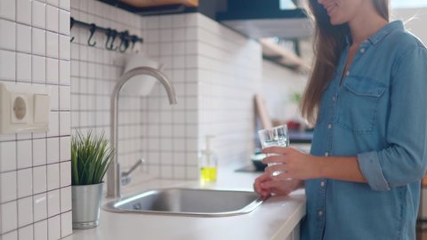 Woman pouring clean filtered water from the tap in glass for drinking at modern loft style kitchen  