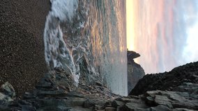 Vertical video. Colorful warm sunset over the sea and volcanic basalt rocks, like in Iceland. The concept of perfect place for summer travel and rest.