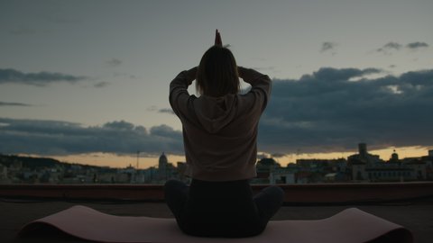 Back View of Young Woman Doing Prayer Pose While Practicing Yoga Home on Roof Terrace Overlooking City at Sunset. Yoga and Meditation Benefits for Mental and Physical Health. Slow Motion Shot