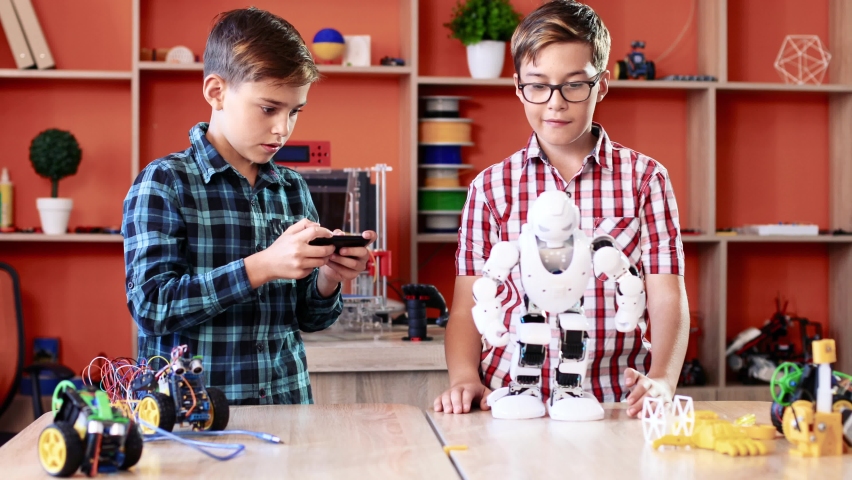 Two boys' classmates are in robotics class. Boy controls robot with digital remote control. Children have fun in class.