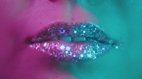 Female lips in neon ultraviolet light. Fashionable neon light, euphoria. Sexy girl licks her teeth with her tongue. Shiny lips in a nightclub. Pink-blue-green color and new light. Metallic lipstick.