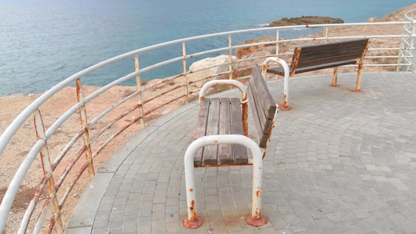 Two white rusty bench on the seashore, on a cliff, which is fenced with a railing. Island of Cyprus. The concept of vacation, relaxation alone, and solitude.