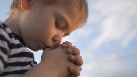 boy prays against a blue sky. child close-up concept faith religion and happy family. kid son jew crossed arms praying to god. worship and gratitude for life and a happy lifestyle childhood. catholic