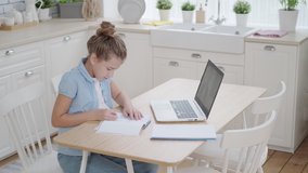 Distance learning online video chat with a teacher. A schoolgirl is studying at home with a tutor making notes in a notebook
