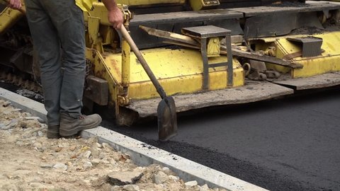 Utility workers collect surplus asphalt behind an asphalt paver. Construction of a new asphalt concrete road.