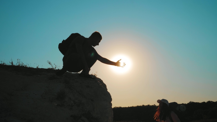 Silhouette of helping hand between two climber. two hikers on top of the mountain, a man helps a man to climb a sheer stone. couple hiking help each other silhouette in mountains with sunlight. Royalty-Free Stock Footage #1062318133