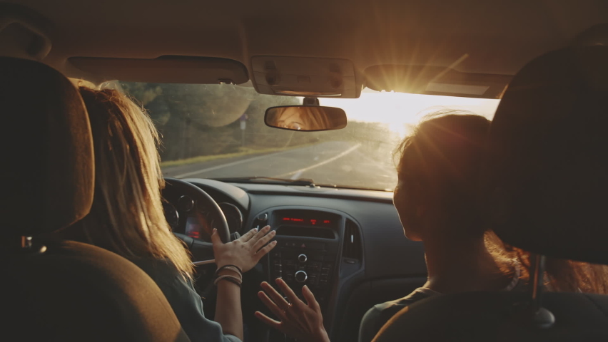 Rear view of cheerful young girlfriends singing their favourite song and dancing while driving at sunset. Two beautiful women travelling and having good time together . Concept of friendship Royalty-Free Stock Footage #1062319567