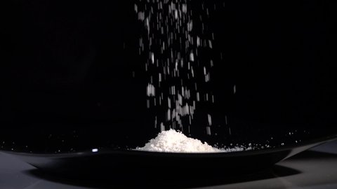 Grated Parmesan cheese falls in slow motion onto a black kitchen plate
