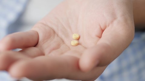 Two small yellow round pills fall into palm of hand from pill bottle. Close-up, front view, center composition