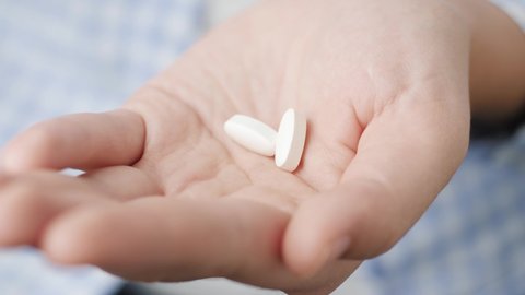 Two big white pills oval diamond-shaped elongated shapes fall into palm of hand from pill bottle. Close-up, front view, center composition