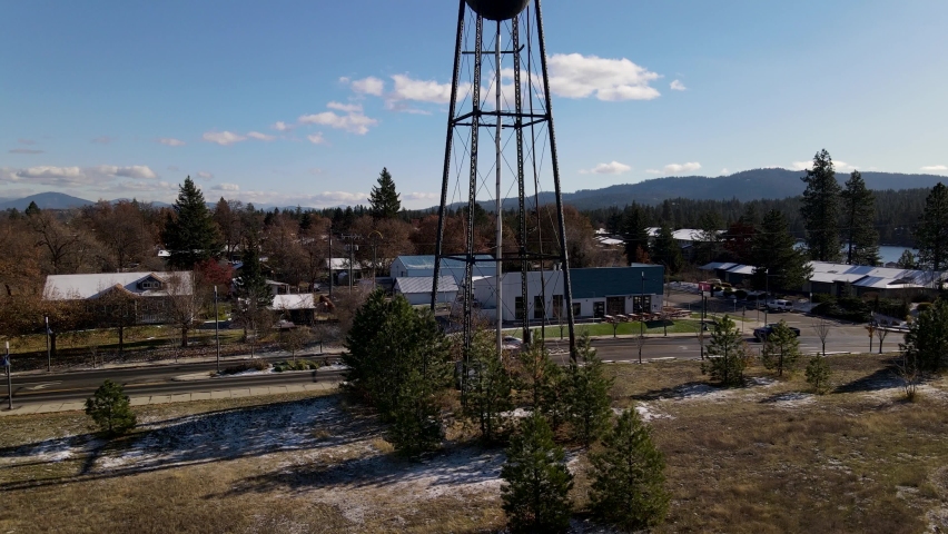 ascending view of a water tower in the small town of Post Falls along the Spokane River in North Idaho on a sunny day with blue sky and houses and mountains in the background.