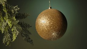 Golden Christmas Ball Hanging On   Tree branch.   Christmas ball toy turning round and back in luminous light on dark green background. 

