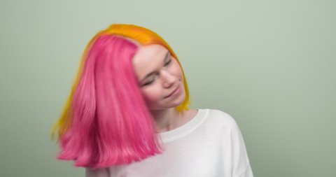  Coloring hair, teenage girl waving bright dyed colored pink yellow hair, hair fluttering on green background. Fashion, hairstyles, trends, hair coloring, youth concept. High quality 4k footage