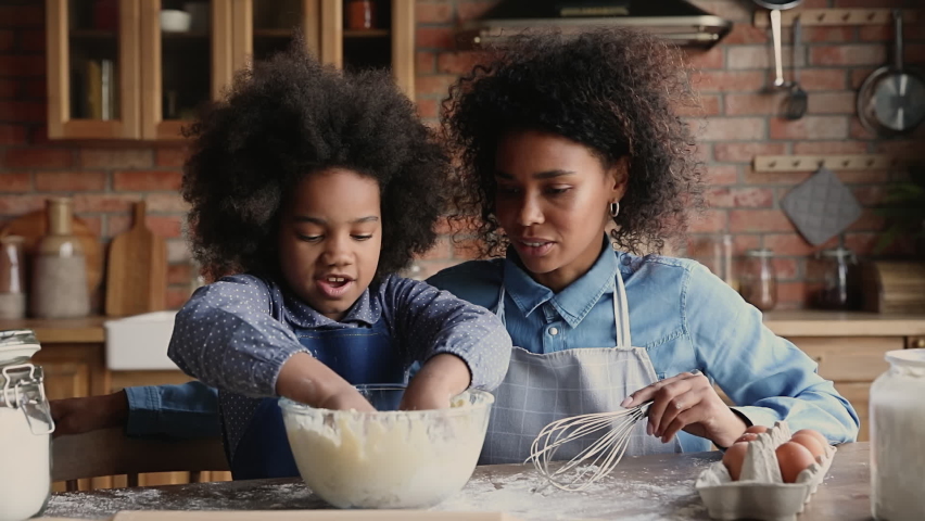 Preschool cute African daughter knead dough cook together with mother in kitchen. Happy loving family preparing holiday dinner for family event celebration. Teaching and developing offspring concept Royalty-Free Stock Footage #1062340897