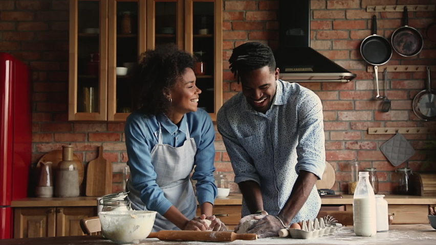 Happy young family African wife and husband standing in cozy kitchen kneading dough cooking together prepare pastries for holiday dinner, celebrate event, enjoy romantic date and communication at home Royalty-Free Stock Footage #1062340903