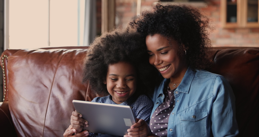 Little girl and mother sit on couch with tablet device. African ethnicity family spend time on internet, enjoy educational web sites for kid development, modern tech usage for fun or education concept Royalty-Free Stock Footage #1062341185