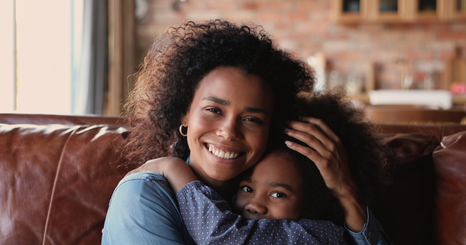 Close up happy african mom and daughter cuddling seated on sofa. Loving parent hug 6s daughter express love, showing caress. Little girl feels grateful embrace new mum. Adoption, Mothers day concept Royalty-Free Stock Footage #1062341194