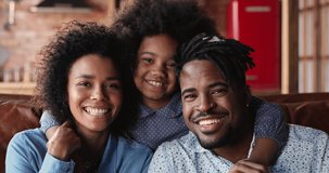 Head shot beautiful african 35s married couple and 6s mixed-race daughter sit on couch hugging smile looking at camera. Close up portrait of happy family, video call remote videochat activity concept
