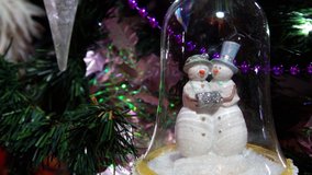 Close up on a snowmen couple in a glass bell jar, hanging on a Christmas tree. A beautiful seasonal ornamental decoration with bright lights