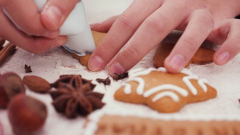 Child hands decorating a pine tree shaped gingerbread Christmas cookie with white icing extreme closeup, camera orbit.
