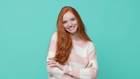 Smiling pretty ginger redhead young girl wearing white pink sweater posing isolated on blue turquoise color background in studio. People lifestyle concept. Looking at camera holding hands crossed - Powered by Shutterstock - Get 15% off with code: PIKWIZARD15