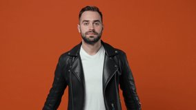 Shocked surprised excited young bearded man 20s wearing casual black leather jacket isolated on orange color background in studio. People lifestyle concept. Looking camera say wow put hands on head